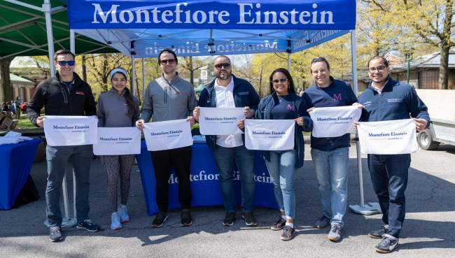 People with Montefiore Einstein towels stand in front of the Montefiore Einstein tent at the race.