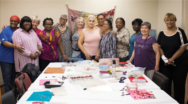 A group of participants in the Bold Living Program stand around a table covered in colorful papers, fliers and crafting supplies.