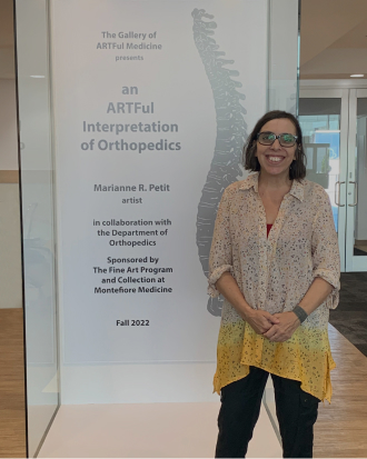 A woman stands next to a floor-to-ceiling sign that reads "An ARTful Interpretation of Orthopedics".