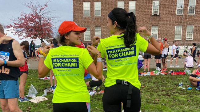 Two runners in "I'm a Champion for CHAM!" T-shirts pose for the camera. The shirts are dayglo yellow with black logos.