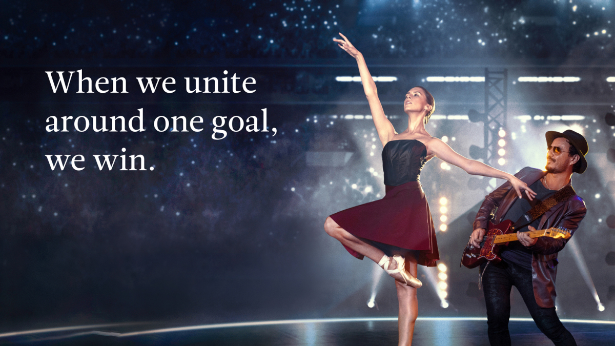 Dressed in a burgundy ballet dress, Chiara dances on a stage. Behind her, an electric guitarist accompanies. Bright lights behind the dark stage give the impression of a star field. On the left, the text "When we unite around one goal, we win."