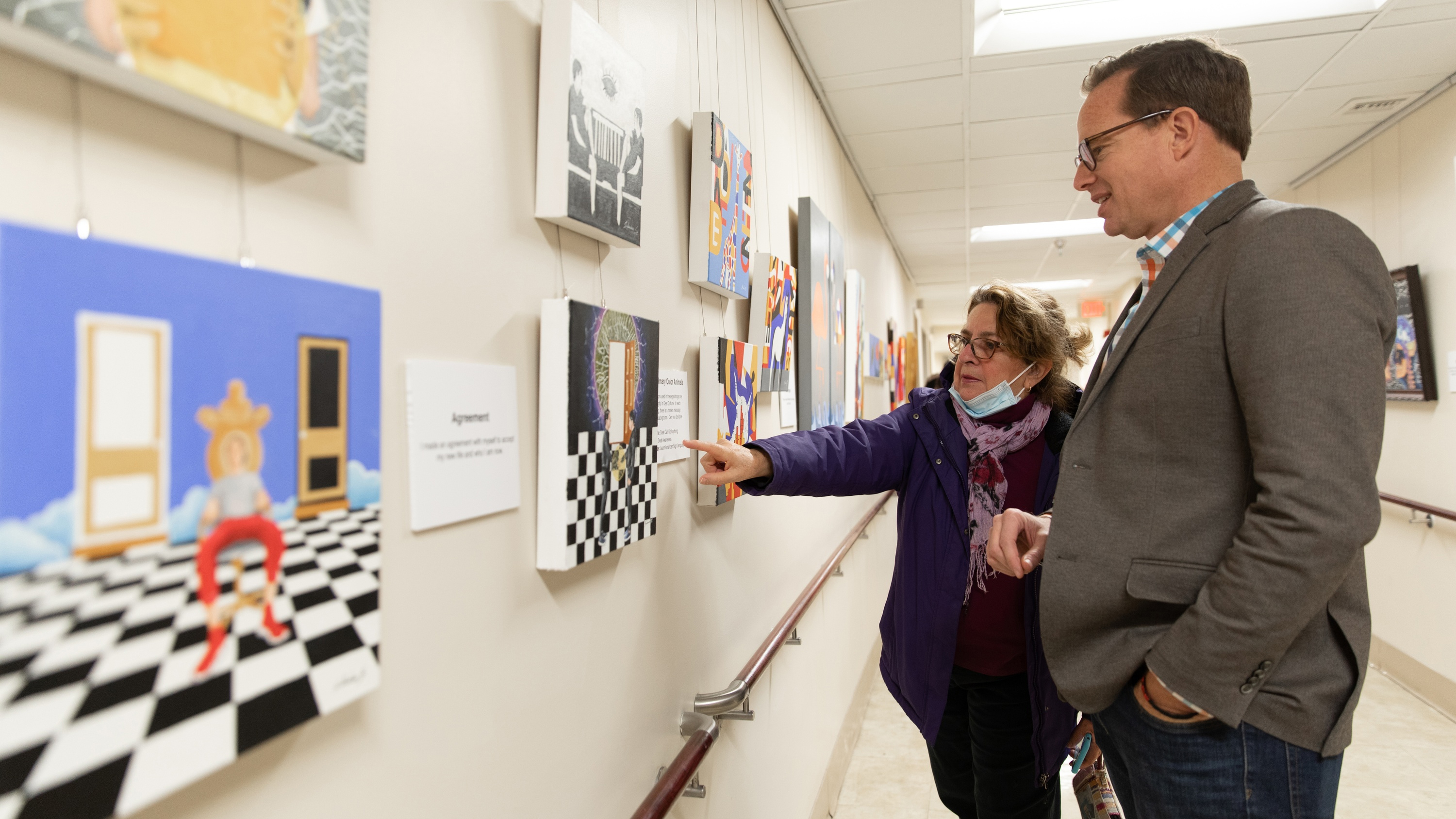 Two gallery-goers discuss Mr. Sanchez' works, pointing to a painting featuring a bold checkerboard in the lower half.