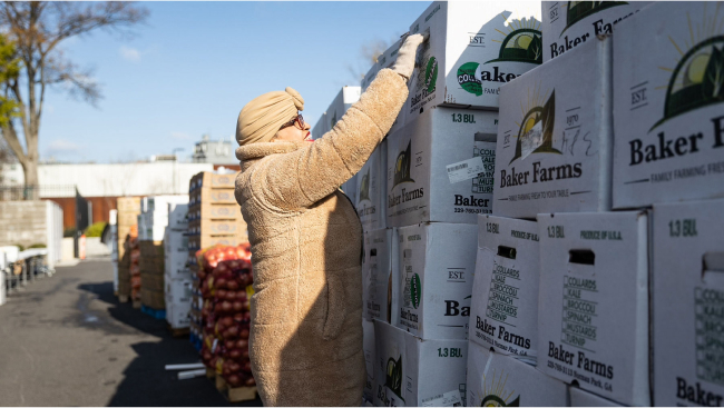 A volunteer pulls down a box of food. They're dressed in a warm winter coat and matching tan hat.
