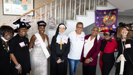 A witch, a beauty queen, a nun, and several other costumed and non-costumed participants come together for a group photo.