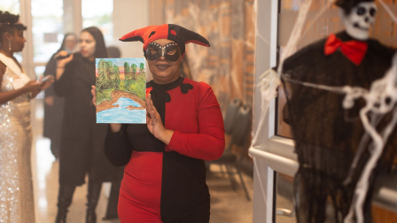 A costumed participant at the BOLD party holds up a painting.