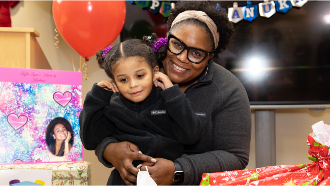 A smiling adult holds a happy child, who is looking down at all the presents.