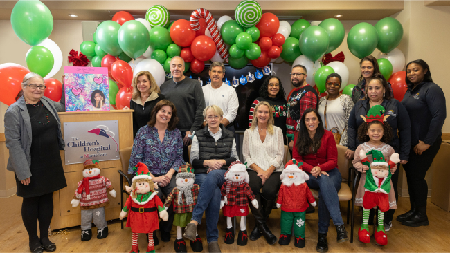 Staffers stand with presents in front of bright red and green balloons.