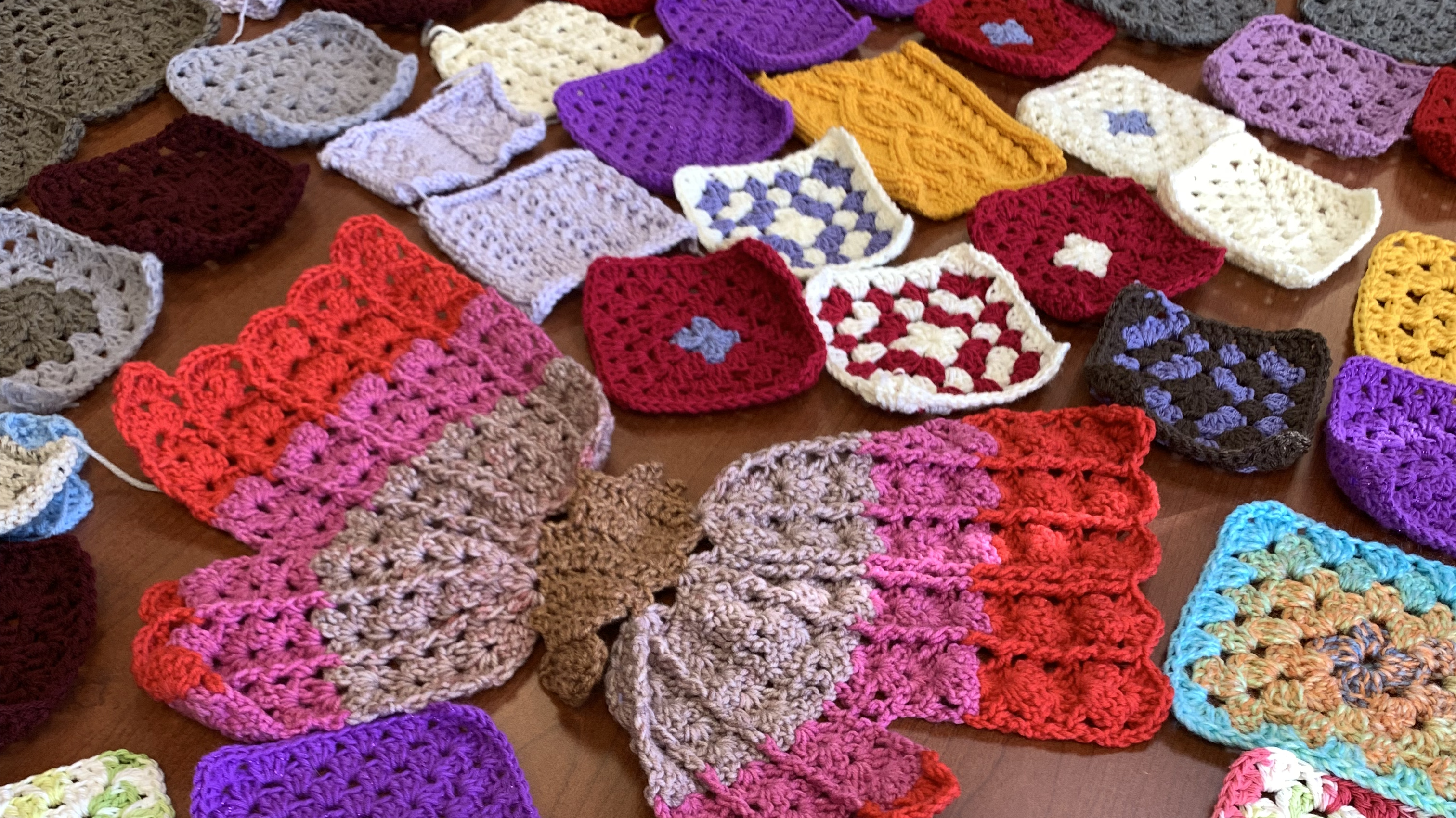 A colorful crochet butterfly in red, purple, tan and brown is centered amid a variety of crochet squares of all colors.