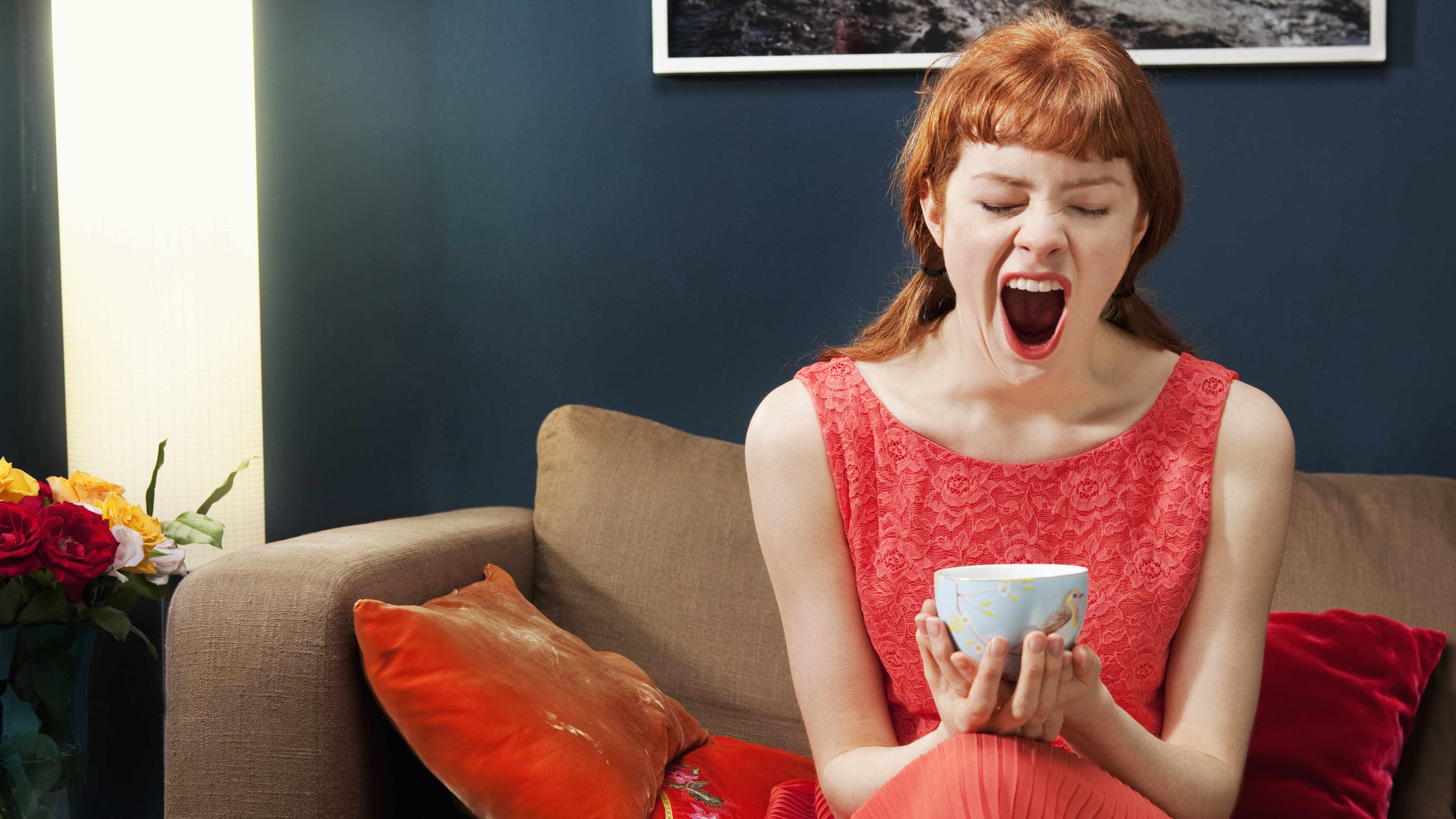 Woman yawning with cup of coffee on her hands