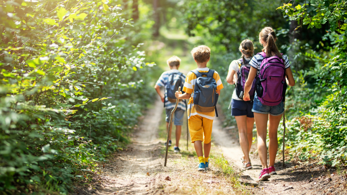 Four kids with backpacks walking down a trail.