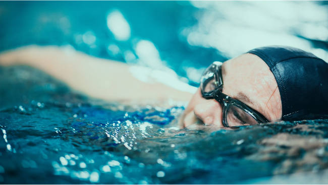Phyllis swims in a pool, wearing a swim cap and goggles.