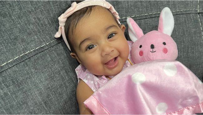 Baby Elsa, smiling under a pink polkadot blanket, hugging a pink bunny.