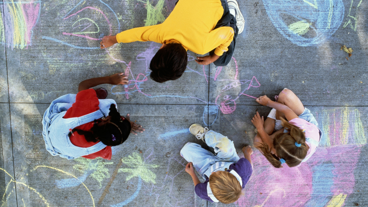 A top down view of children drawing on pavement with sidewalk chalk.