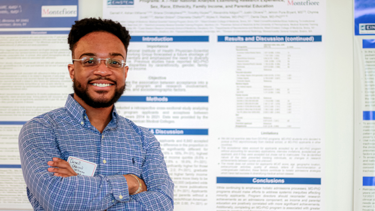 A student smiles proudly in front of a large scientific poster.