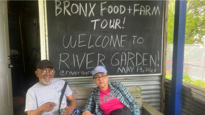 Two participants enjoy the shade in front of the River Garden chalkboard during the Bronx Food & Farm Tour.