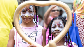 Smiling children with facepaint, framed by a golden heart-shaped ballon.