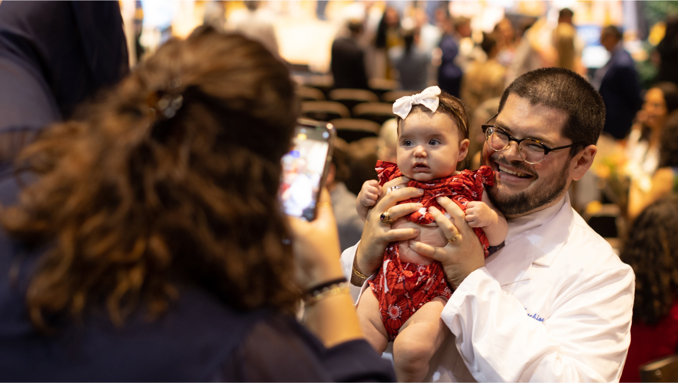 A proud white coat recipient holds up a baby for a picture.