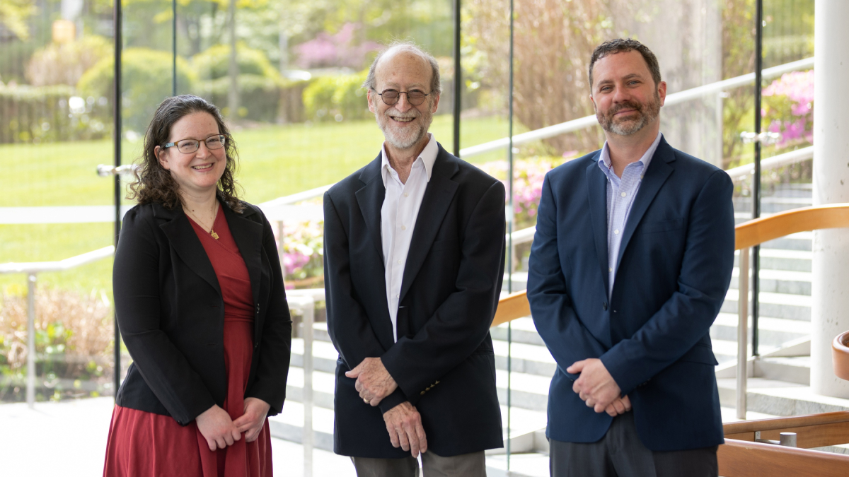 Three members of the Montefiore Einstein School of Medicine and Montefiore Health System team stand, smiling, in front of a glass wall with a view of a green courtyard.