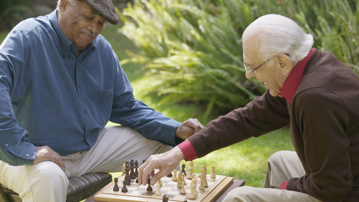 Two older men play chess in a park.