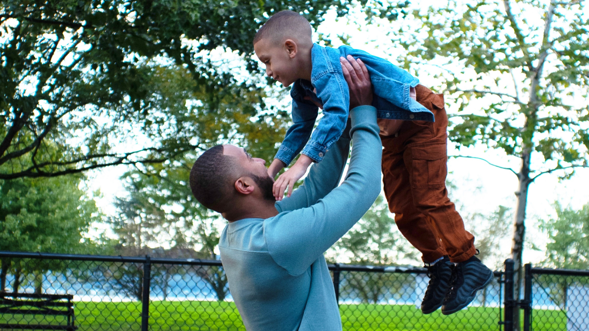 A photo of a man holding up a toddler in an outdoor park.