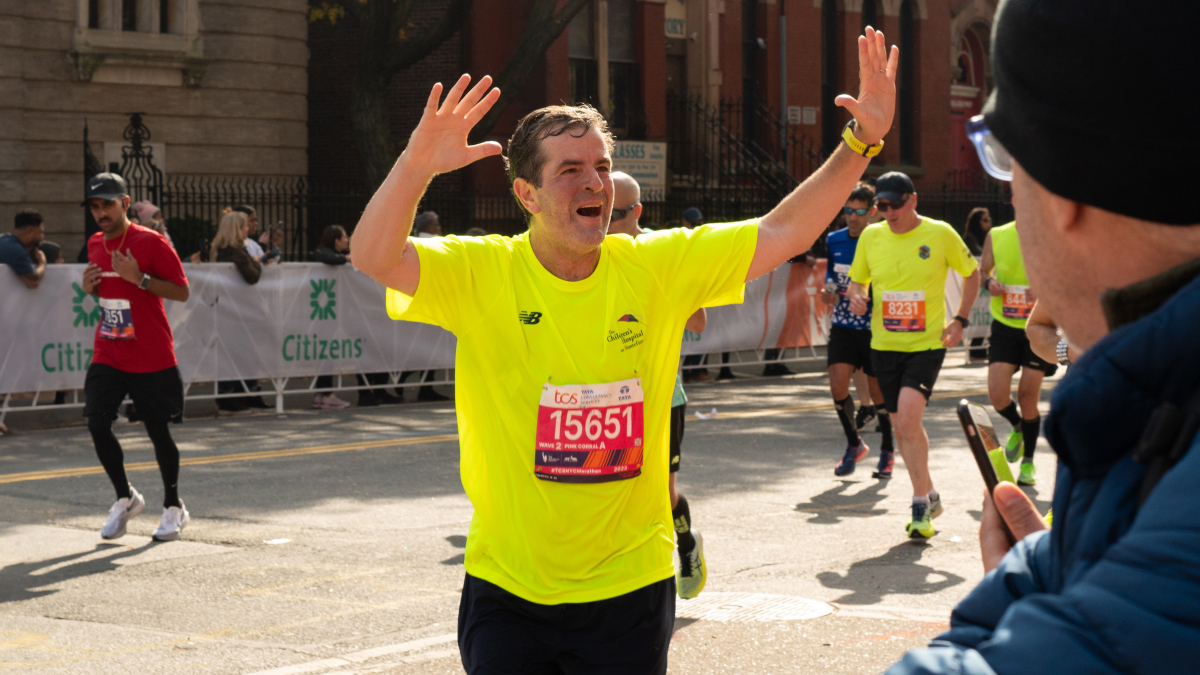 A marathoner runs, arms raised in a victorious pose.