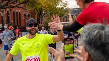A marathoner in a yellow shirt high-fives a person on the sidelines.