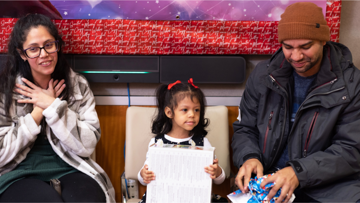 A smiling family helps a little one open her presents.