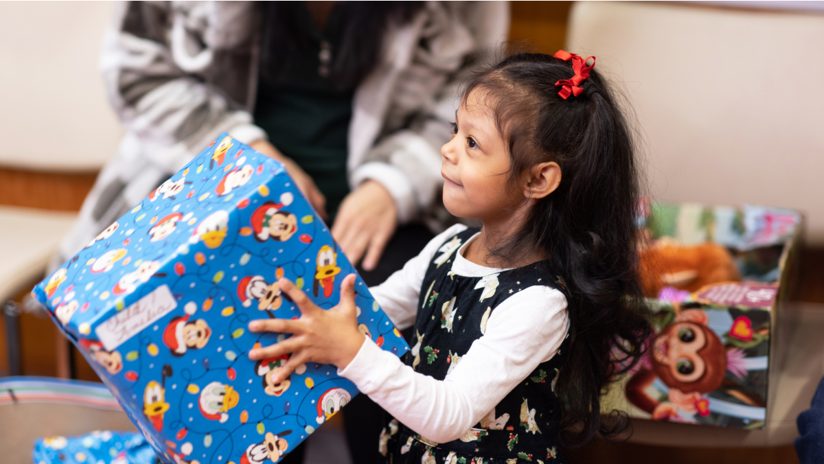 A little girl, smiling, holds up a wrapped package.