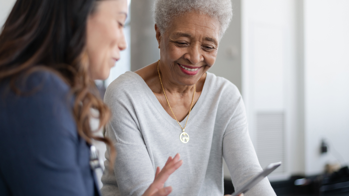 A young woman shows an older woman how to use her tablet.