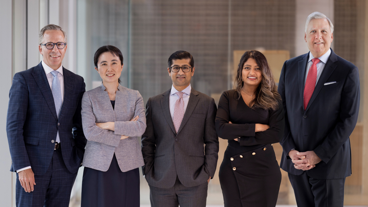 Five doctors in business dress pose for a group photo.