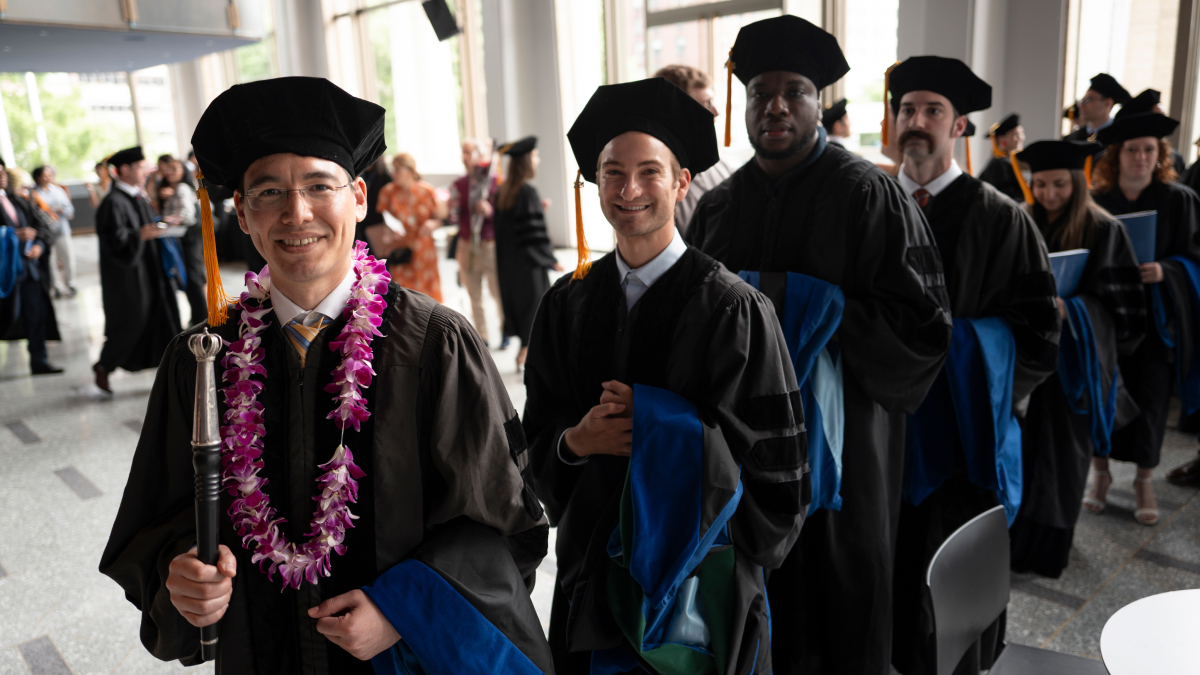 A line of smiling students in robes line up for Commencement.