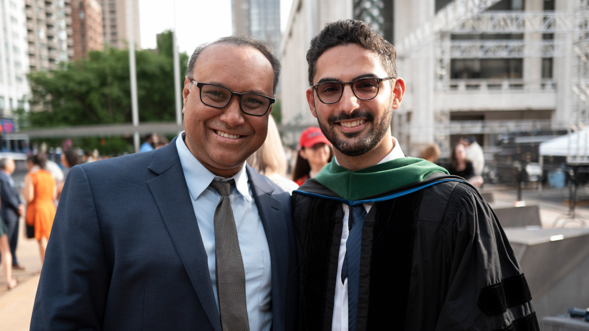 A graduate stands beside a man in a suit, both smiling toward the camera. 