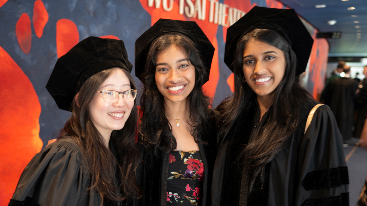 Three smiling students pose for a picture wearing caps and gowns.