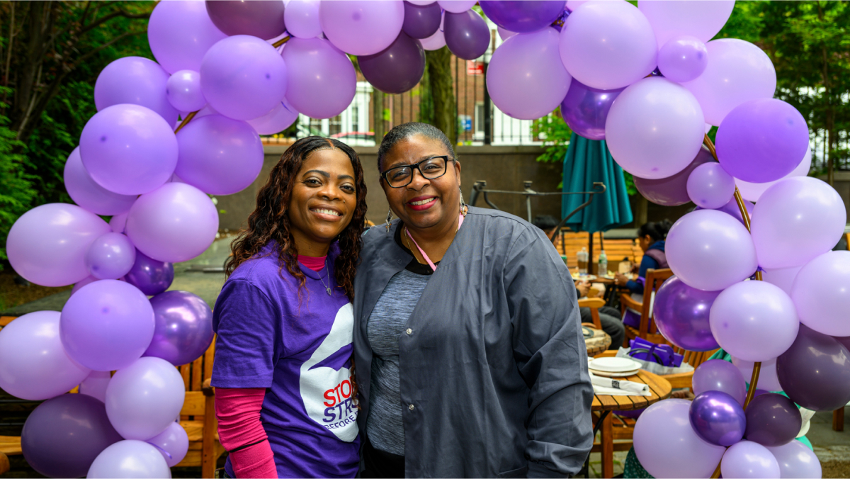 Happy attendees pose for a photo under the lavender and purple balloon arch.