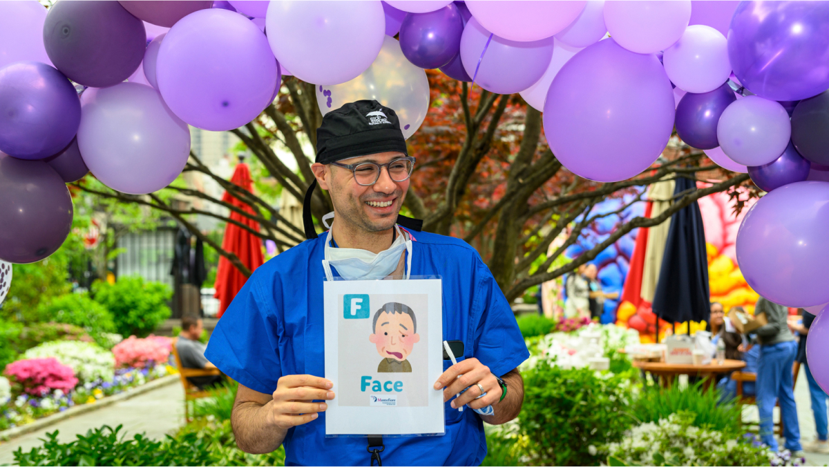 A participant holds up a poster under the lavender and purple balloon arch.