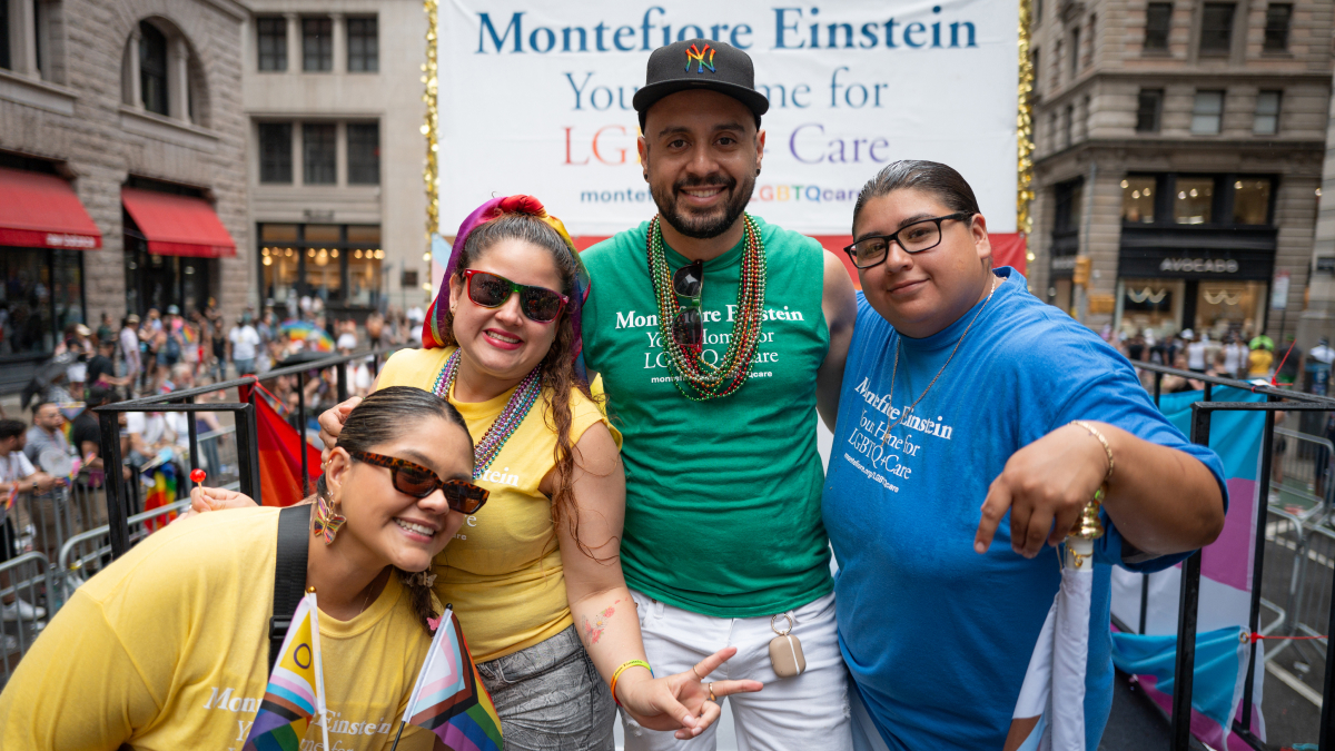 Four happy parade goers pose for a photo in front of the Montefiore Einstein banner.