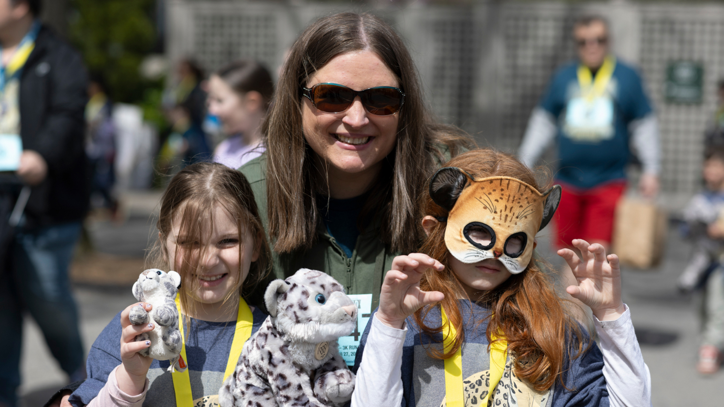 Children, one with stuffed snow leopards and another in an animal mask, smile and pose for a picture with their grown-up.