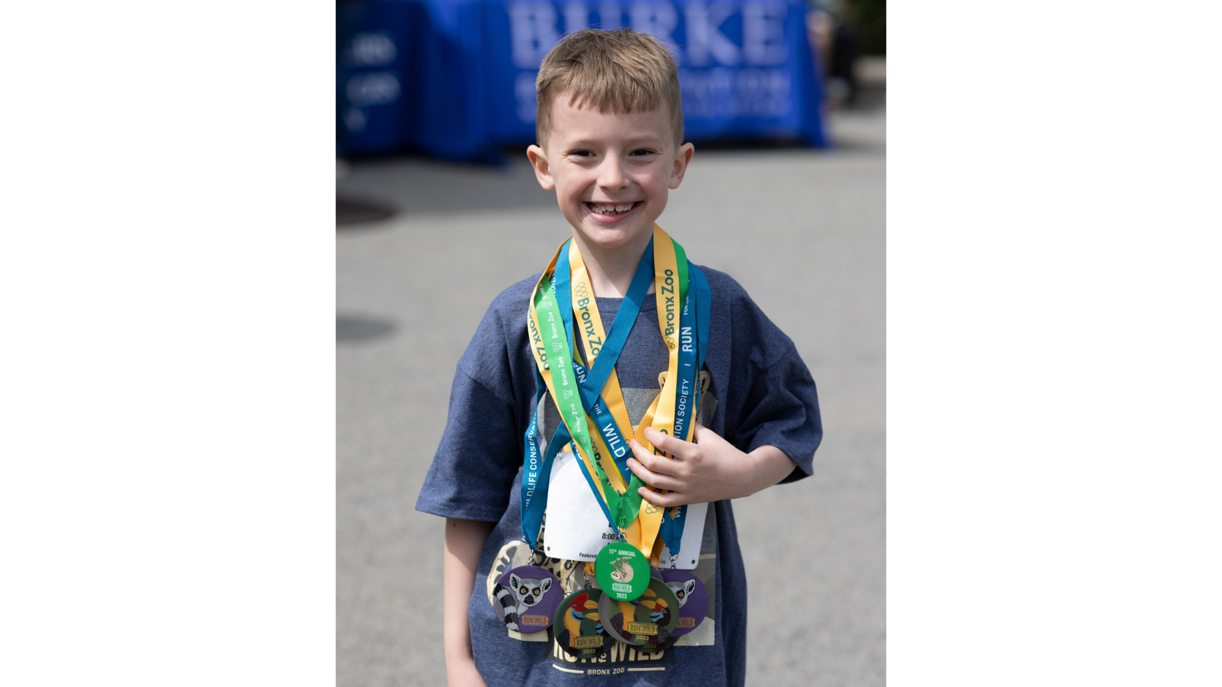 A young boy draped in running medals smiles broadly for a picture.