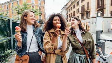 Three happy young women dressed for a brisk day enjoy ice cream cones on a city street.