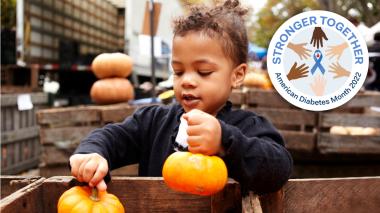 An adorable child chooses two small pumpkins from a pumpkin bin. 