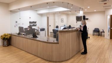 A staffer stands next to a large wooden admitting desk in a clean modern medical office.