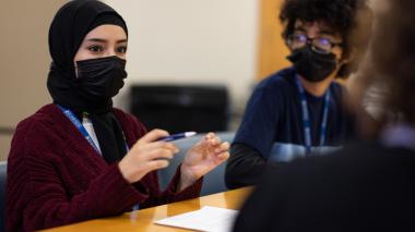 A diverse group of students sit around a table talking.