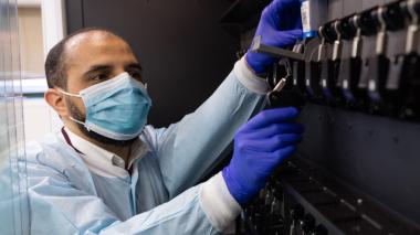 A masked scientist in protective gear runs a test.