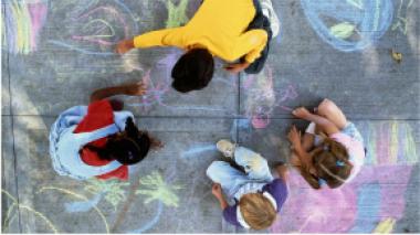 A top down view of children drawing on pavement with sidewalk chalk.