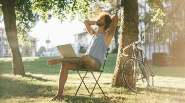 A man sits outdoors in a chair with his laptop enjoying the sunshine