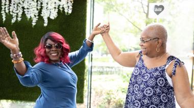 Two participants celebrate BOLD beauty day, arms held open wide, big smiles.