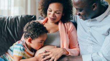 A family, with the child kissing the mother's pregnant belly in a sweet scene.