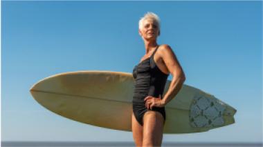 A woman stands in front of the ocean holding a a surfboard.