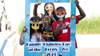 Five children in animal masks stand behind a cardboard frame that reads "Family Diabetes Day at the Bronx Zoo 2023". 