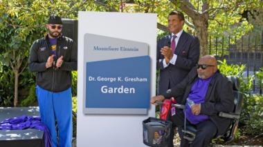 Dr. Gresham and Dr. Ozuah and others stand beside the new sign for the Dr. George K. Gresham Garden.
